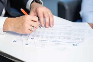 image of hands holding a pen on sheets of data; analysis in problem solving