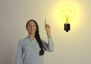 woman with braid holding up hand and index finger against white background, image of lightbulb to upper right of woman; soft skills matter: creativity