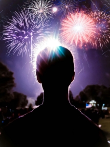 silhouette of an adult head in foreground, colorful fireworks in background against night sky; 4th of July - why do we celebrate?